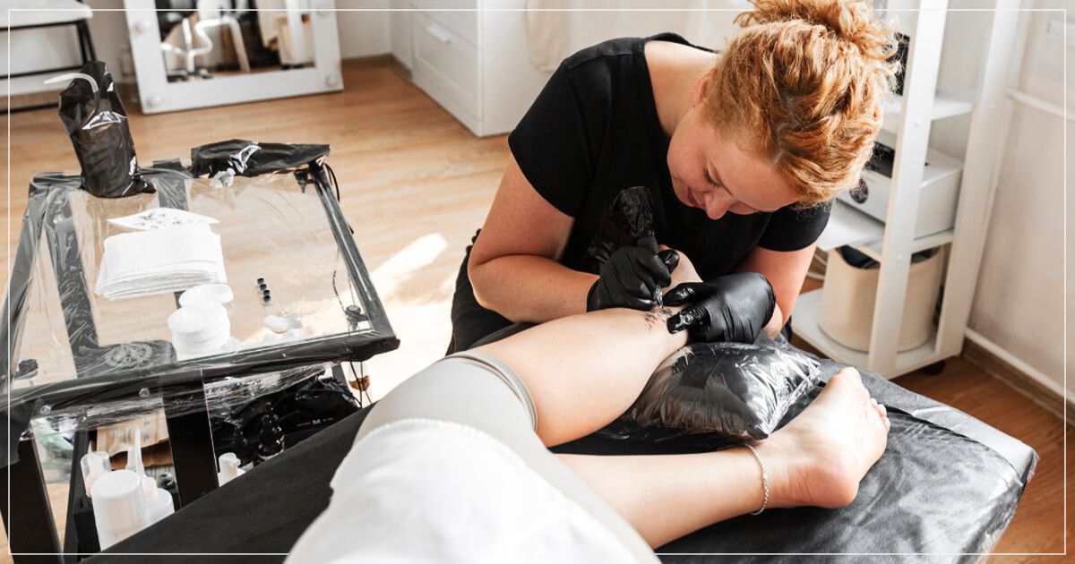 Female tattoo artist tattooing leg.